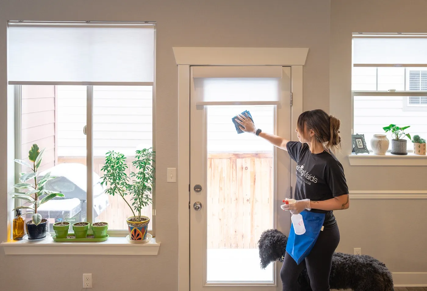 A Dashing Maids cleaner wiping a glass door in a bright Denver home