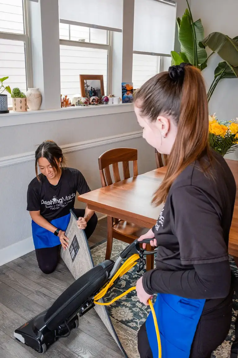 Two cleaners lifting a rug corner to vacuum underneath